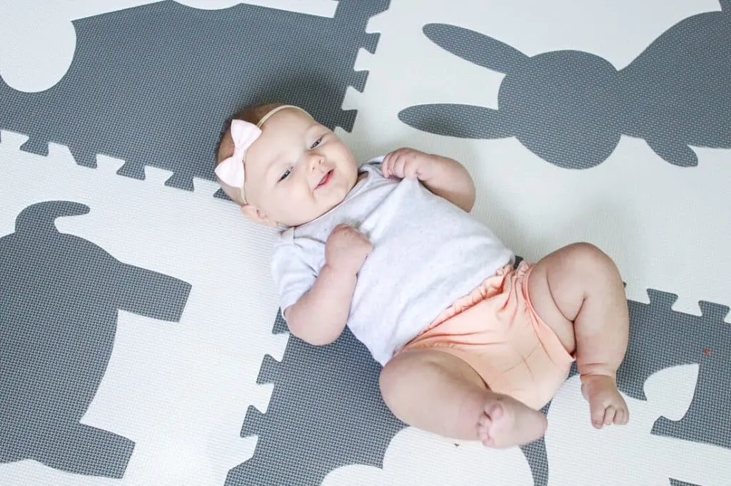 baby plays on play mat and smiles at camera.