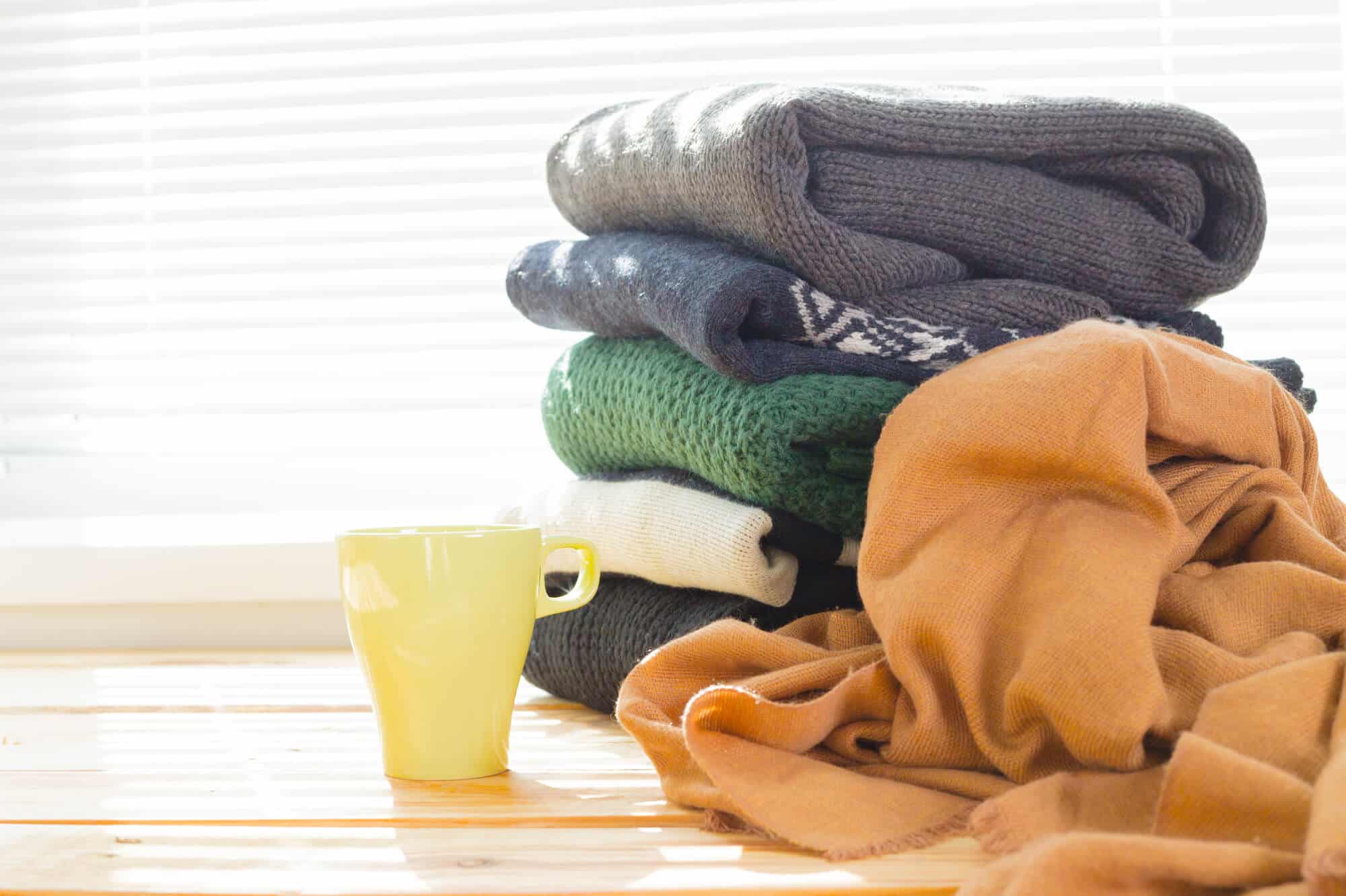 Stack of sweaters next to coffee cup.
