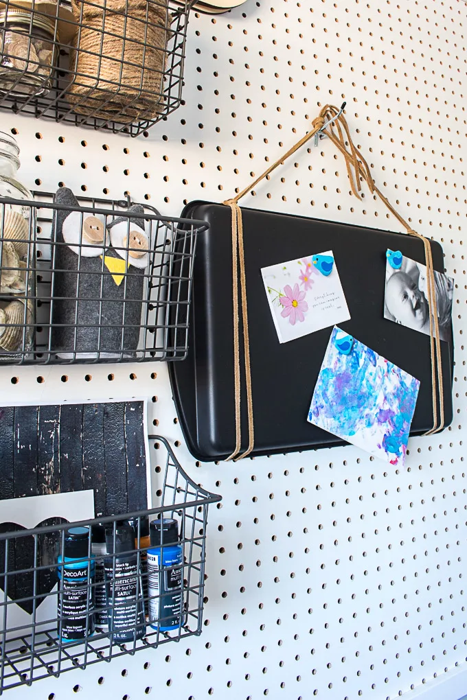 An old sheet pan painted with chalk paint with cards attached by magnets hanging on a peg board.
