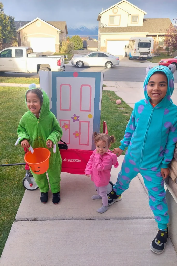 Siblings dresses as the Monsters from Monster's Inc and Boo in front of a wagon with a cardboard door.