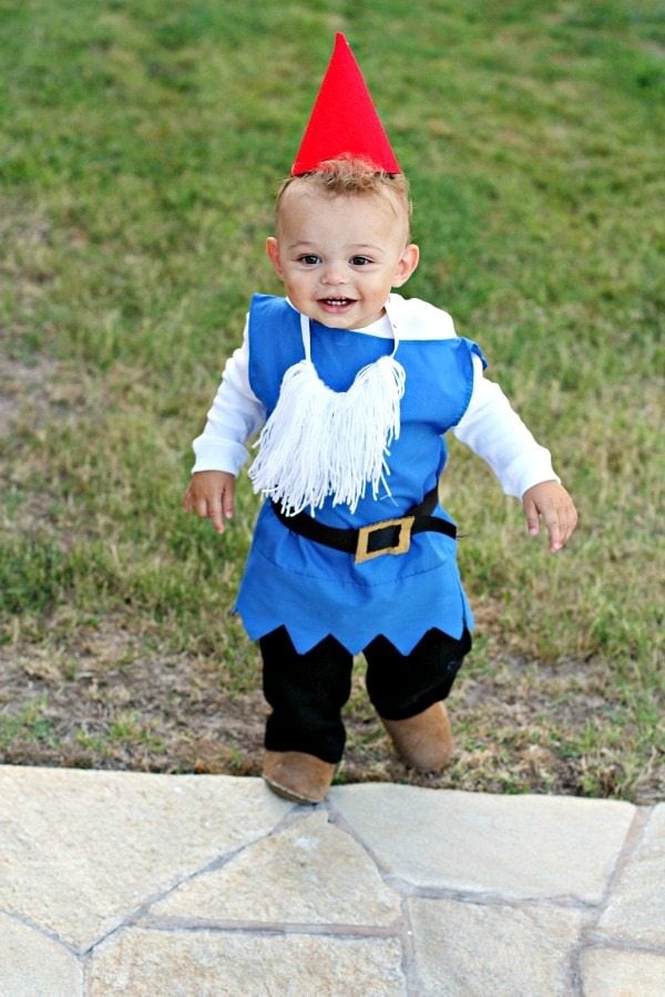 A little boy dressed as a garden gnome with a blue top, black pants, and red hat.
