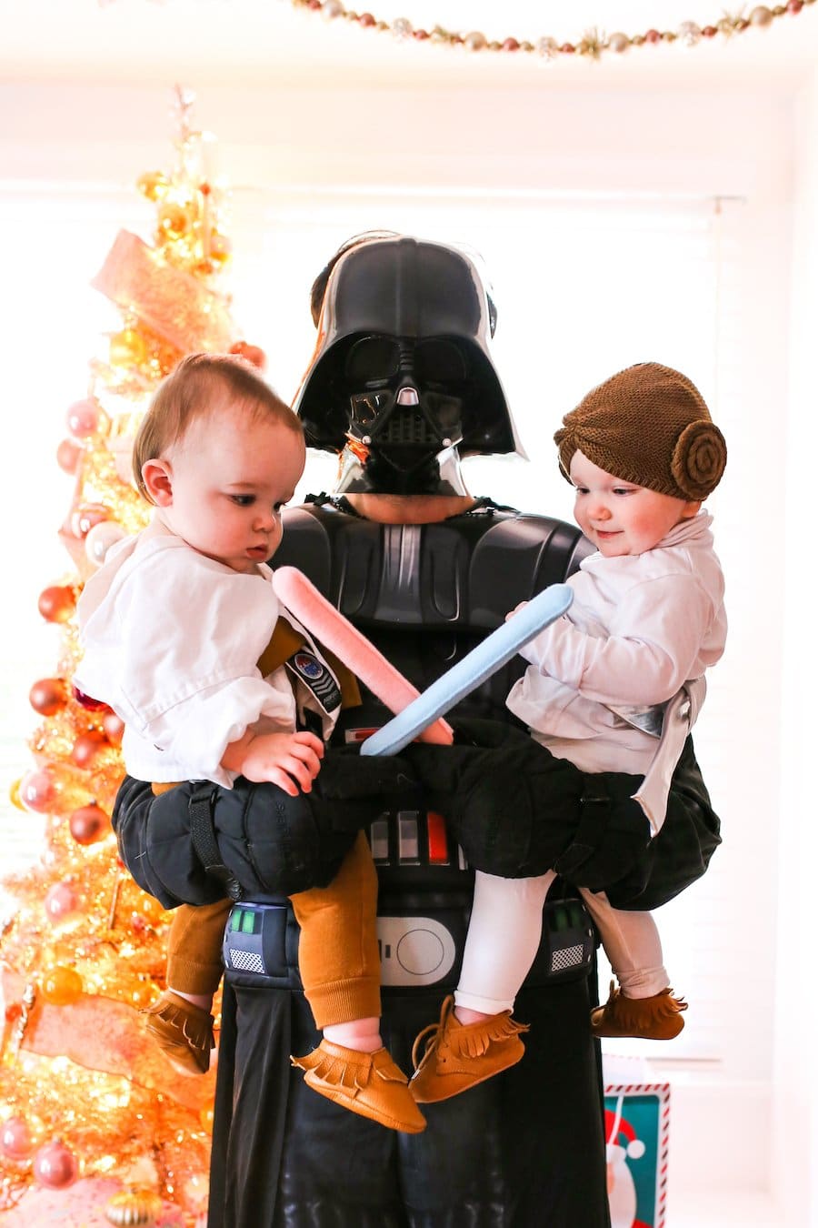 Twin babies dressed up as Luke and Leia from Star Wars held by Darth Vader.