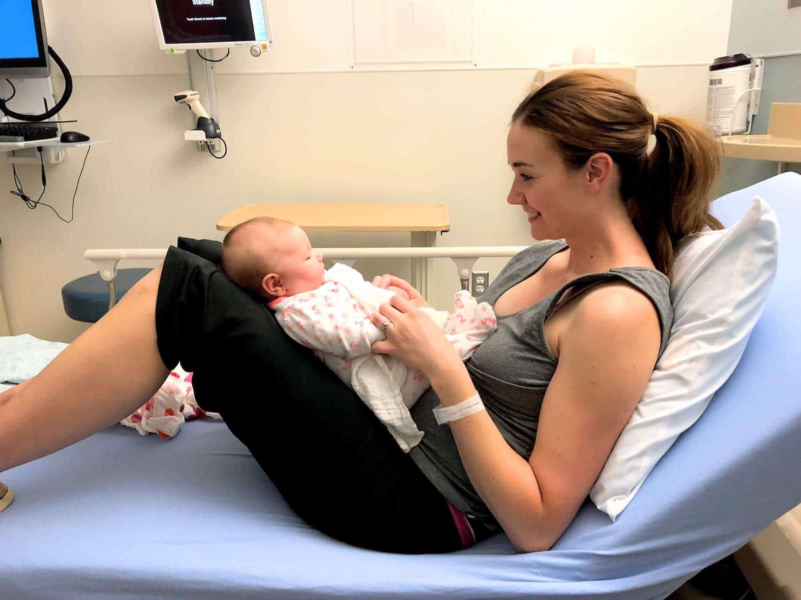 Woman holds baby on hospital bed in medical facility.