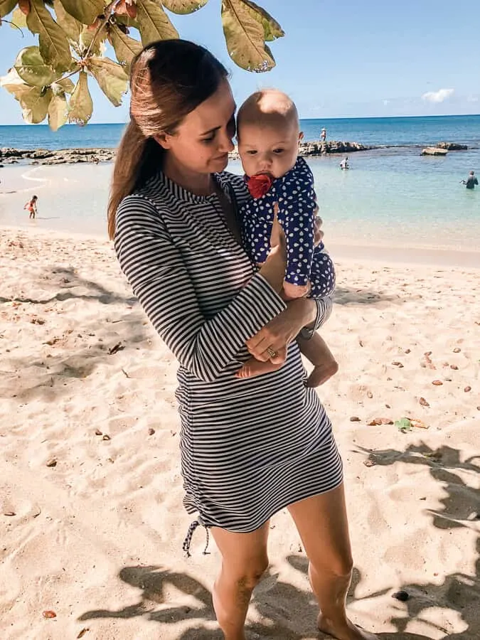 Mother holds baby on family beach in Oahu.