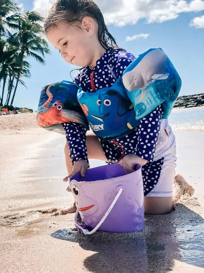 Girl plays with bucket at hidden beach in Hawaii.
