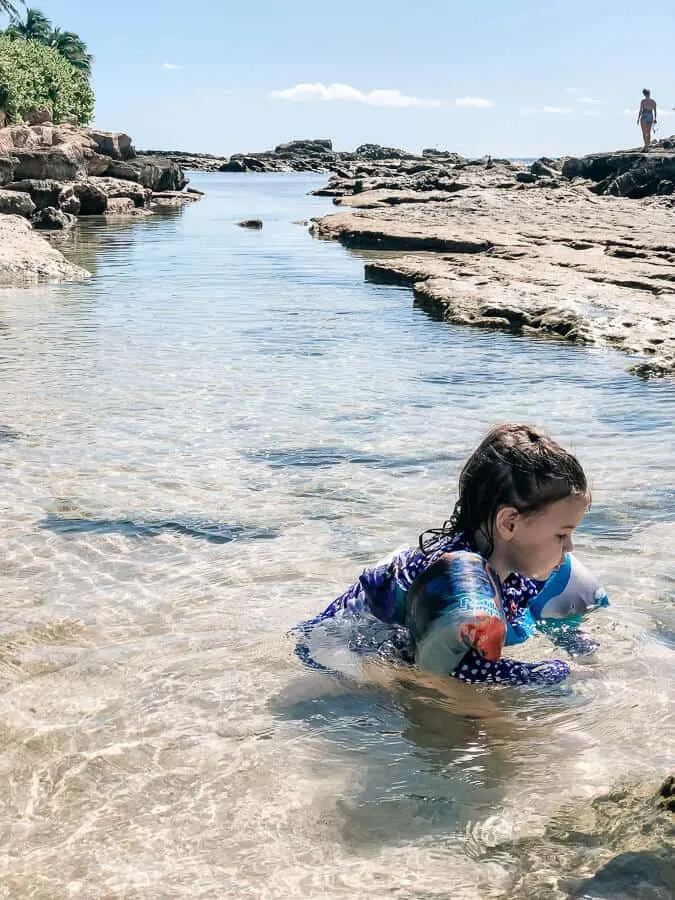 Girl plays in water channel at Oahu beach for families.