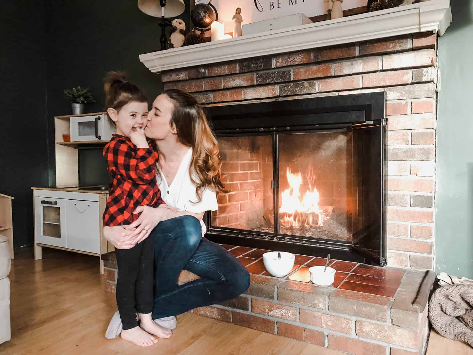 Mom hugs child next to cozy fireplace.