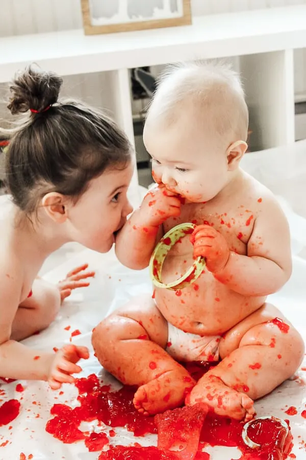 Toddler and baby eat red Jello during play time.