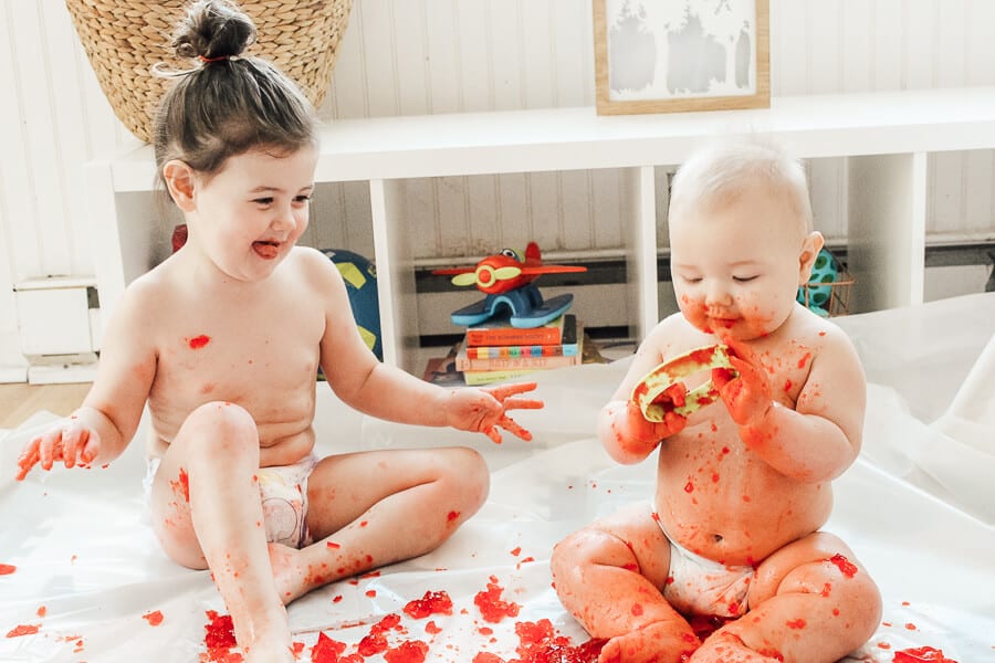 Children play with red Jello in diapers.