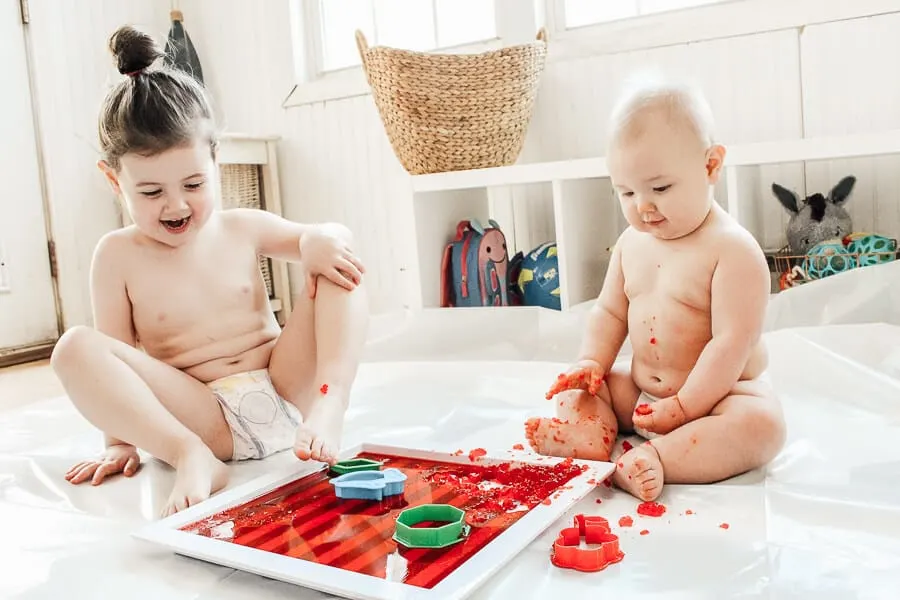 Toddler and baby stimulate their senses with Jello play.
