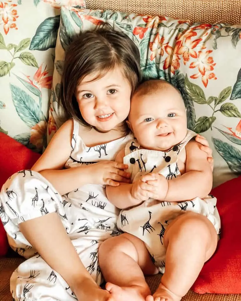 Toddler girl and baby sit on couch at Aulani Resort.