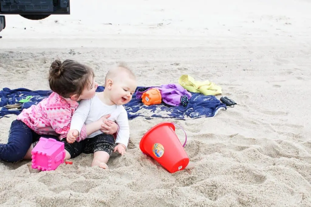 Toddler girl and baby play at beach.