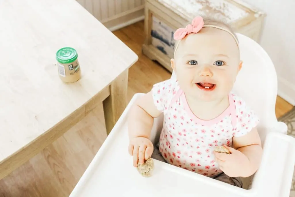 Baby eats baby food muffins in high chair.