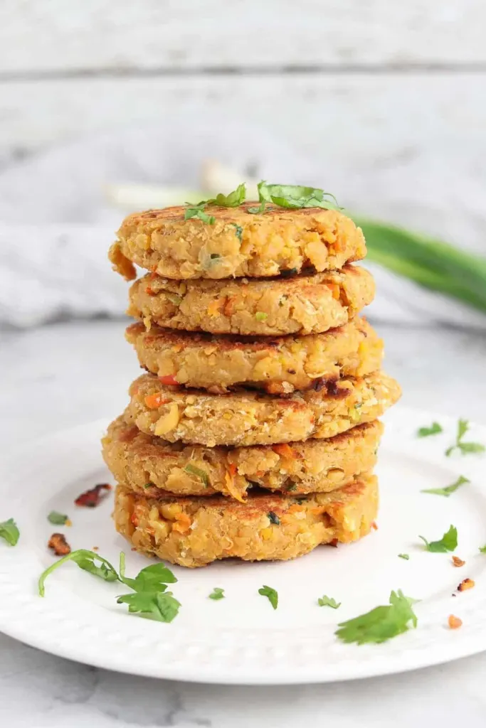 A stack of chickpea patties on a white plate with green garnish sprinkled on top.