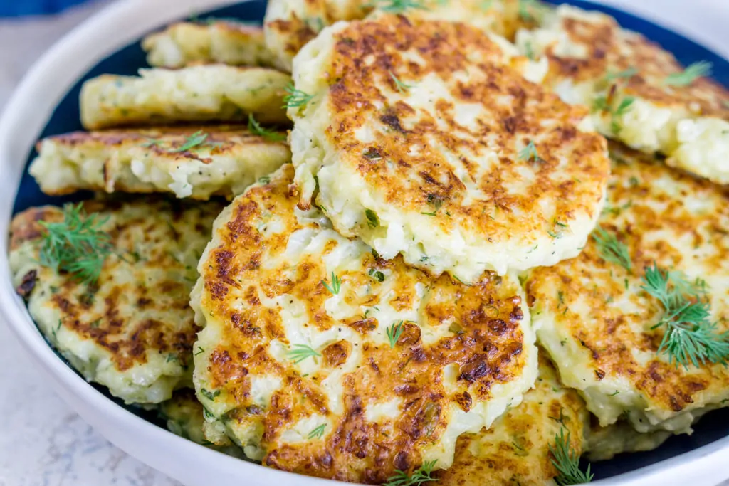 A large bowl of fried cauliflower fritters with green garnish on top.