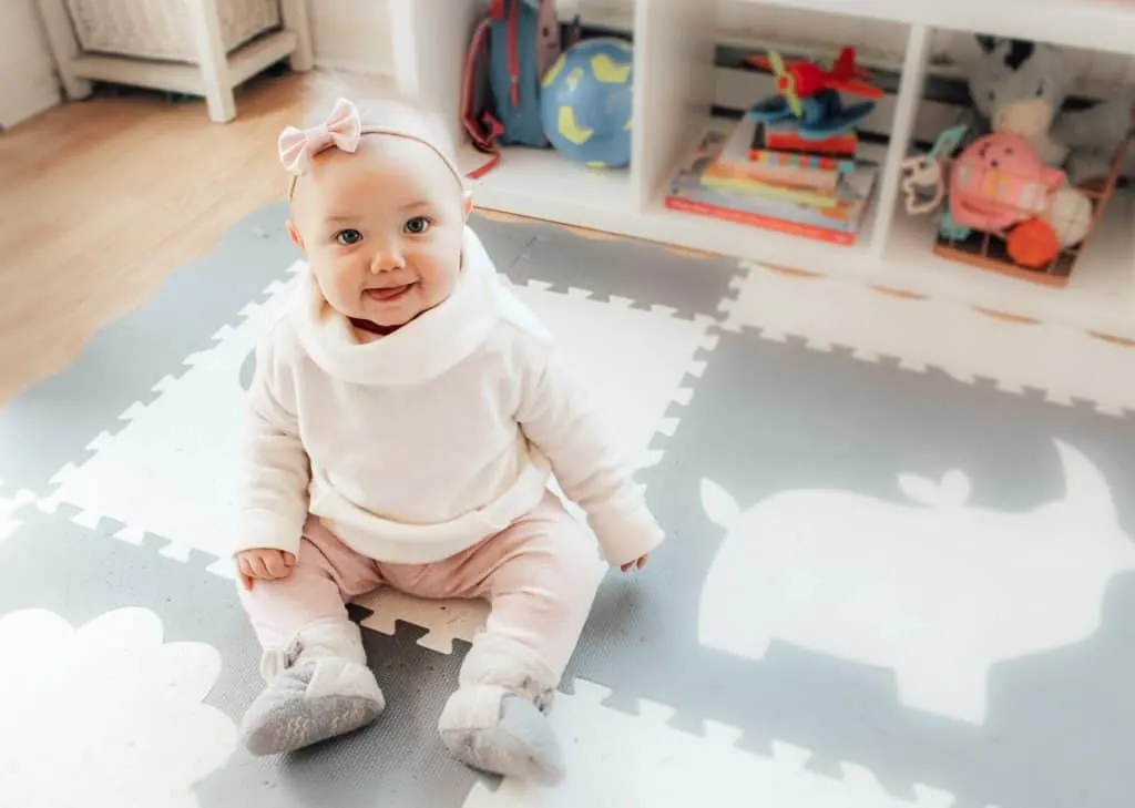 Baby girl sits on playroom floor.