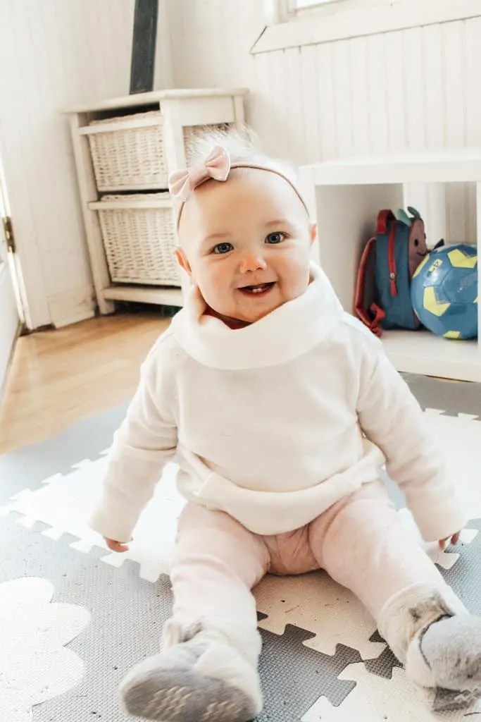 Baby girl sits on playmat in playroom.