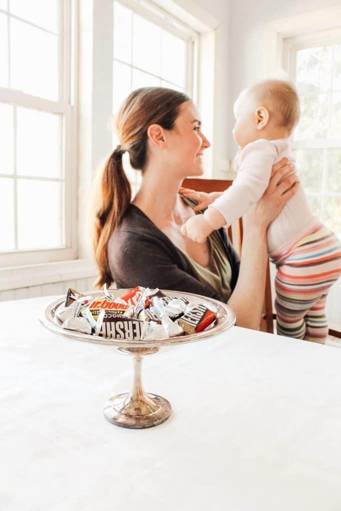Woman holds baby next to tray of treats.