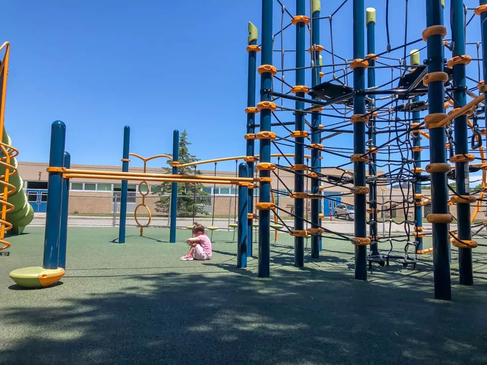 Child sits next to playground ropes course.