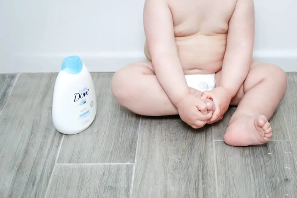 Baby sitting on floor with Baby Dove Rich Moisture Lotion bottle