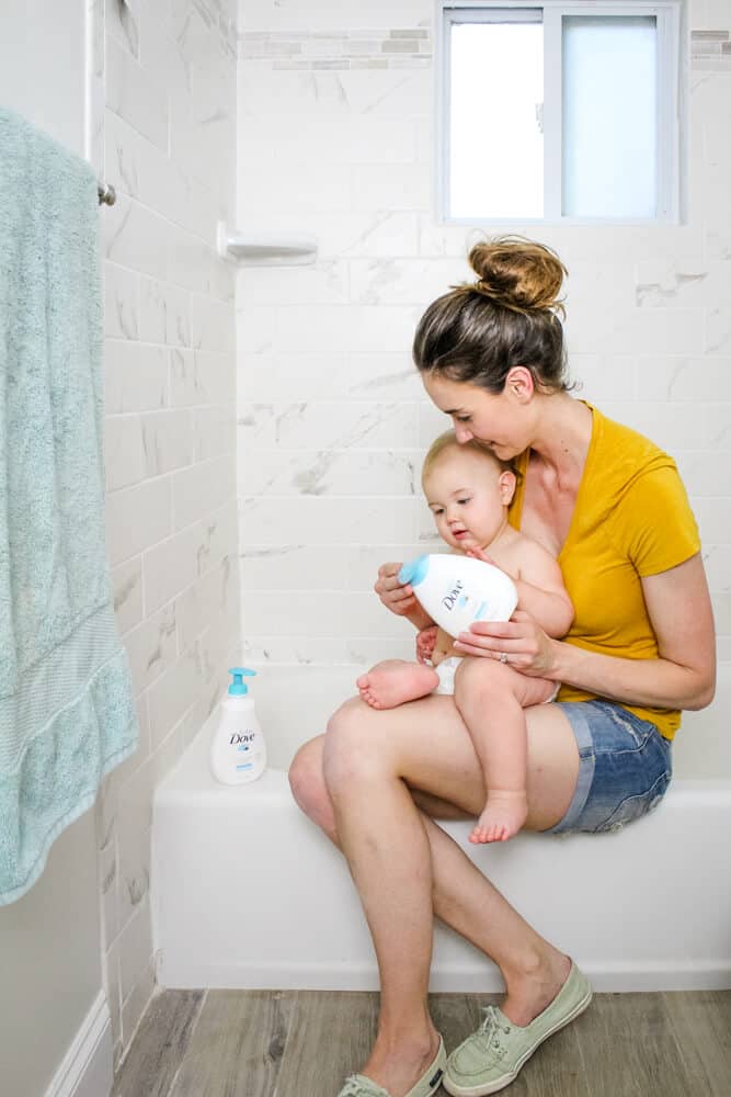 Mom and baby sitting on edge of bathtub with Baby Dove Rich Moisture products