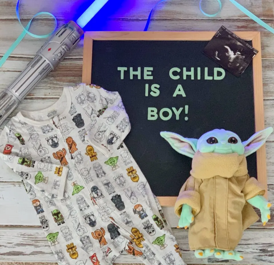 Flat lay Mandalorian gender reveal with a letterboard "baby Yoda" and Star Wars onesie.