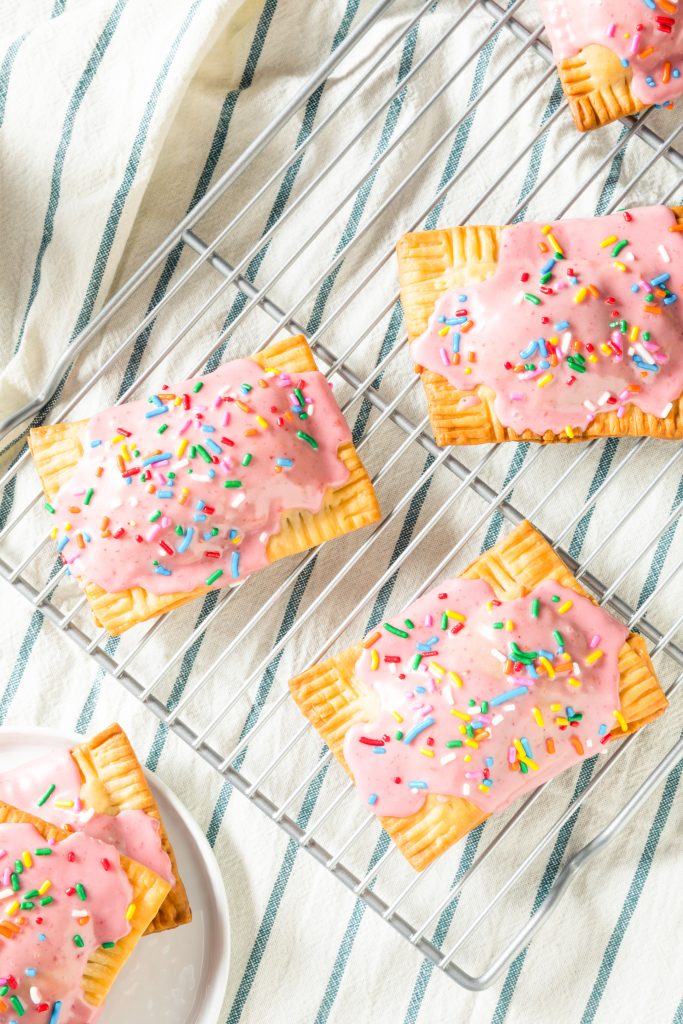 Homemade pop tarts with pink icing and sprinkles on a cooling rack.
