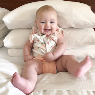 Baby sits on bed propped up by pillows.
