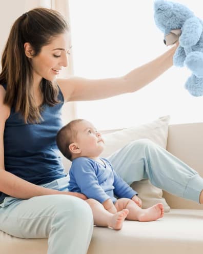 Woman holds teddy bear above observant baby.