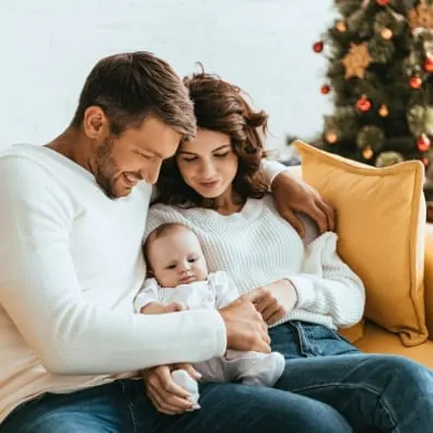 New parents hold baby next to Christmas tree.