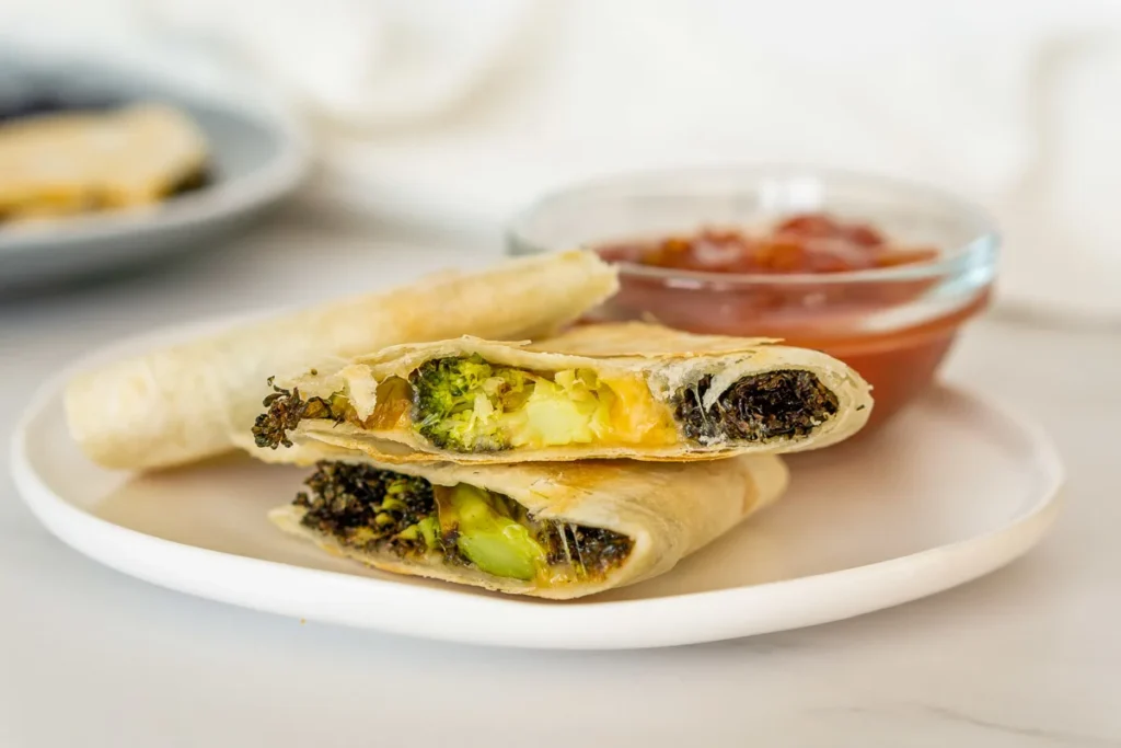 Broccoli and cheese quesadillas on a plate with red dipping sauce.