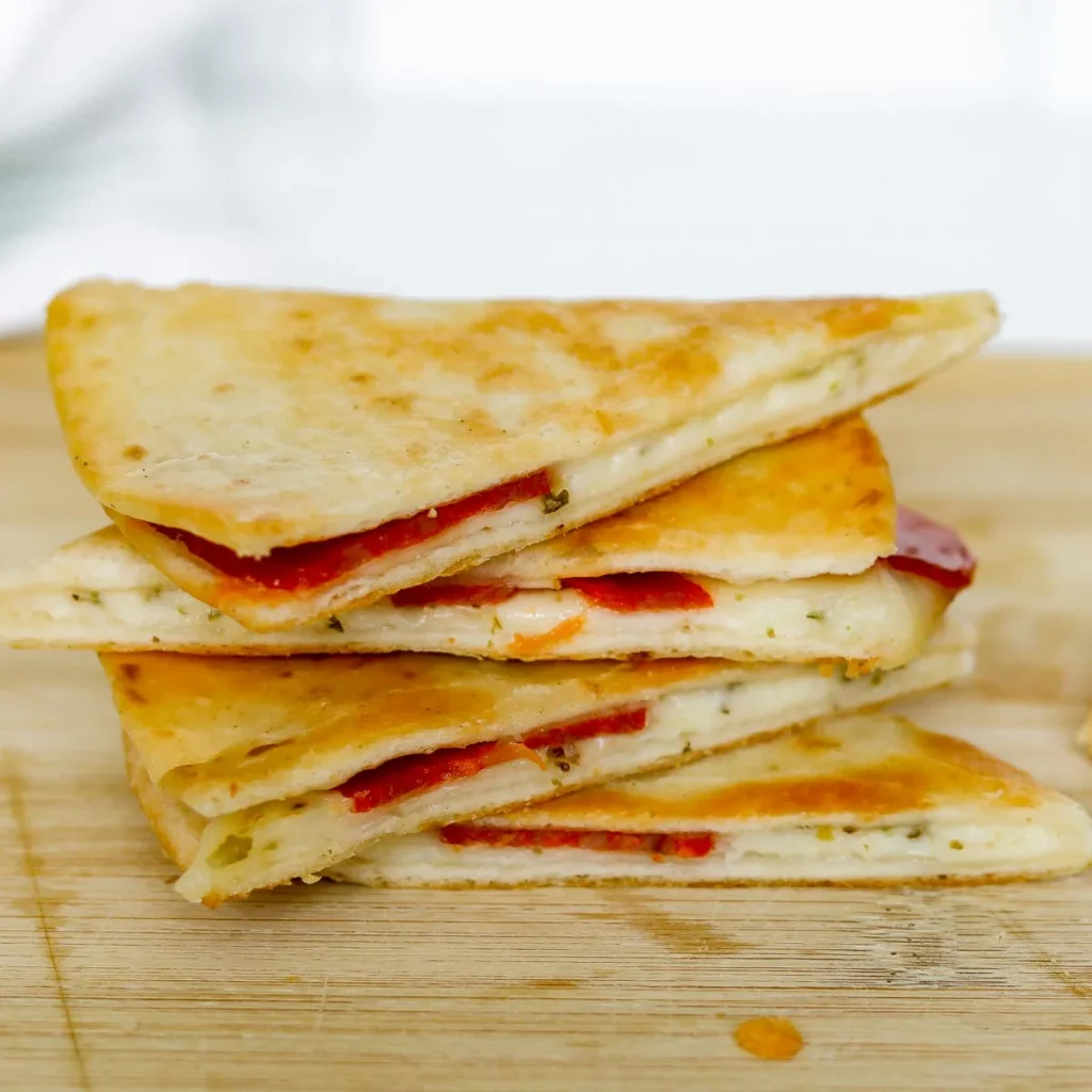 A stack of pizza quesadillas on a wooden cutting board.