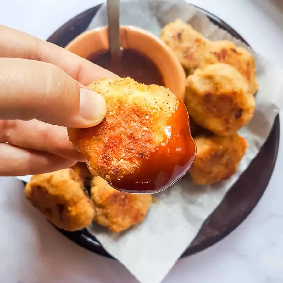 A woman holds a sweet potato chicken nugget with ketchup on it.
