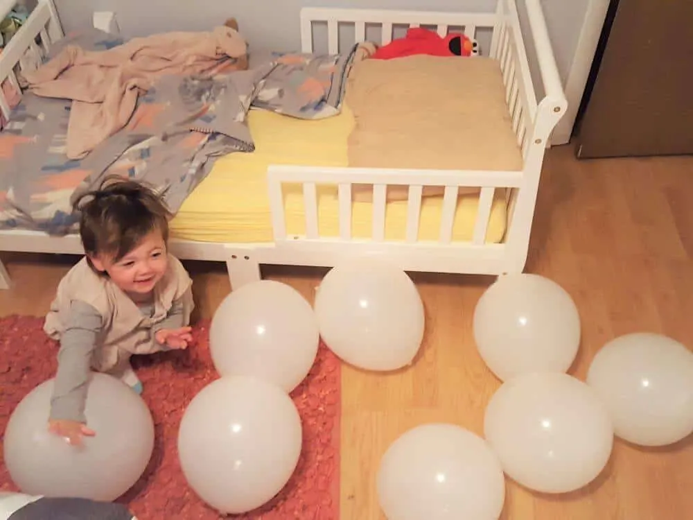 Child plays with balloons on bedroom floor to celebrate her at home birthday.