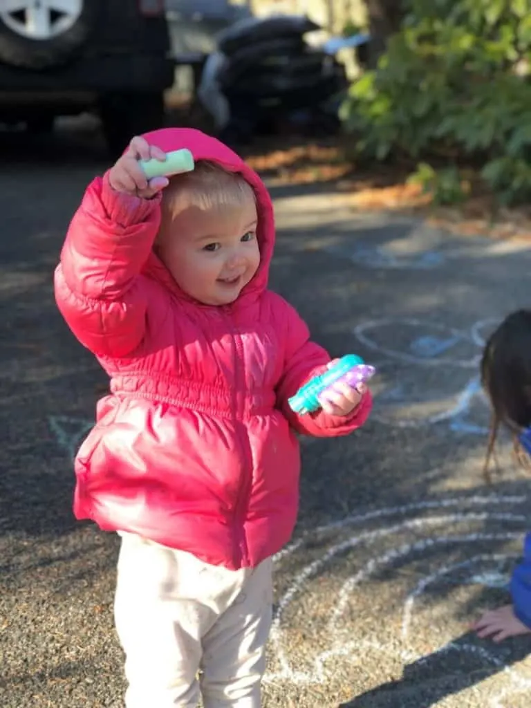 Toddler girl holds sidewalk chalk while celebrating birthday at home.