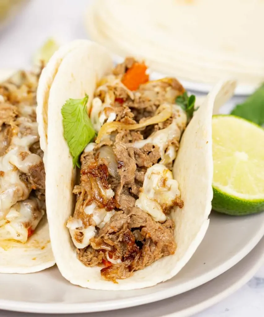 Philly cheesesteak tacos on a white plate with slices limes.