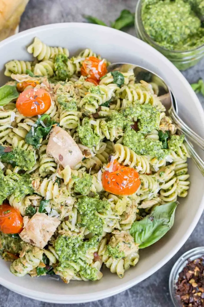 Tuna pasta salad with pesto sauce and tomatoes in a white bowl.