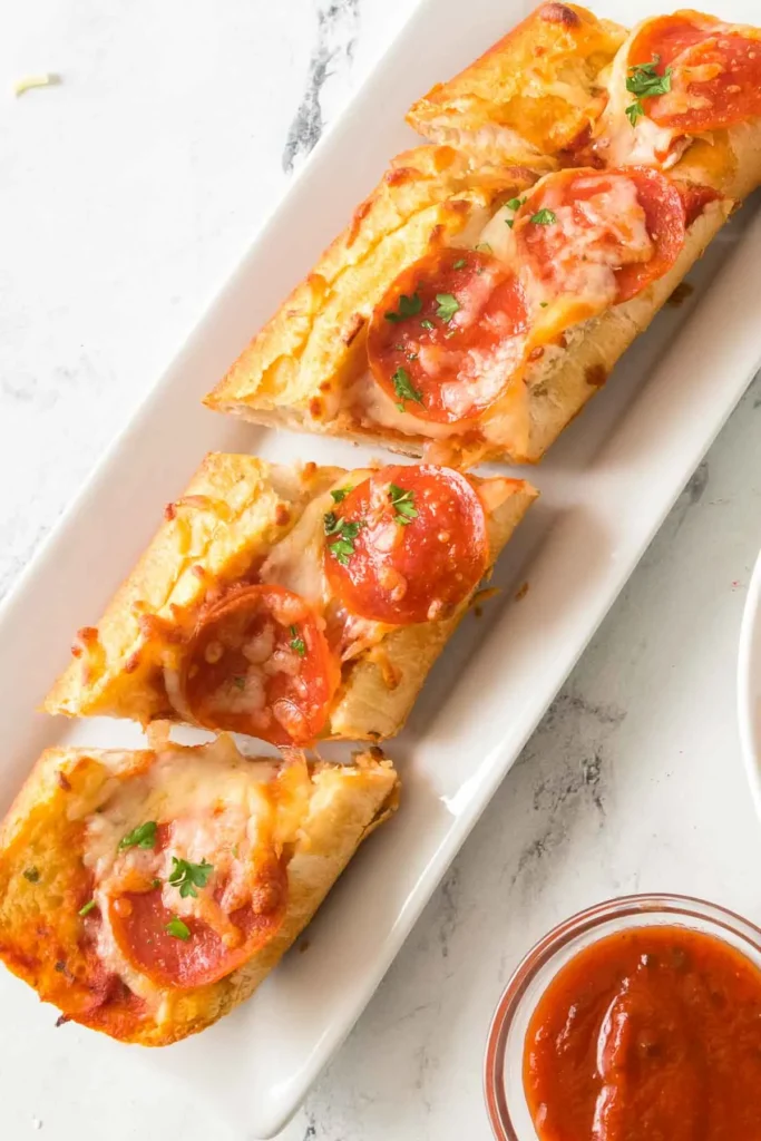 Sliced garlic bread pizza on with pepperoni on a white serving platter with marinara dipping sauce.