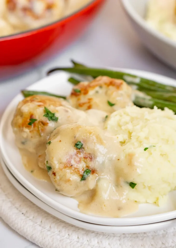 Chicken Swedish meatballs with gravy, mashed potatoes, and green beans on a white plate.