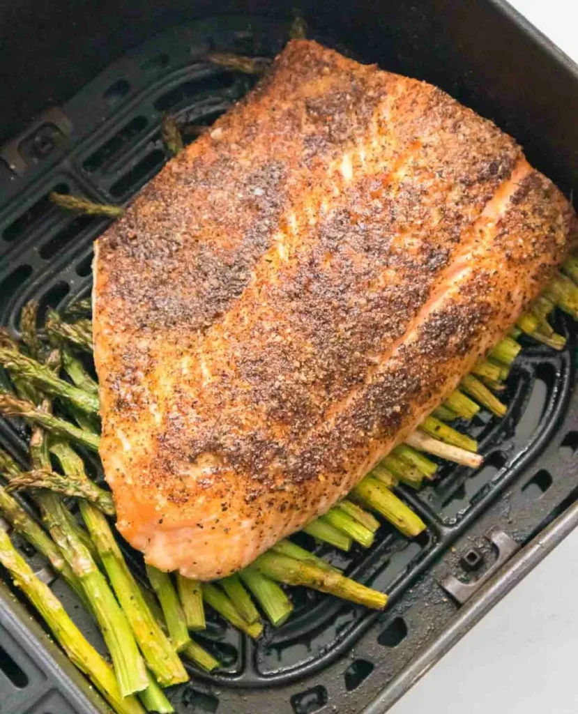 An air fried salmon filet over asparagus in an air fryer basket.