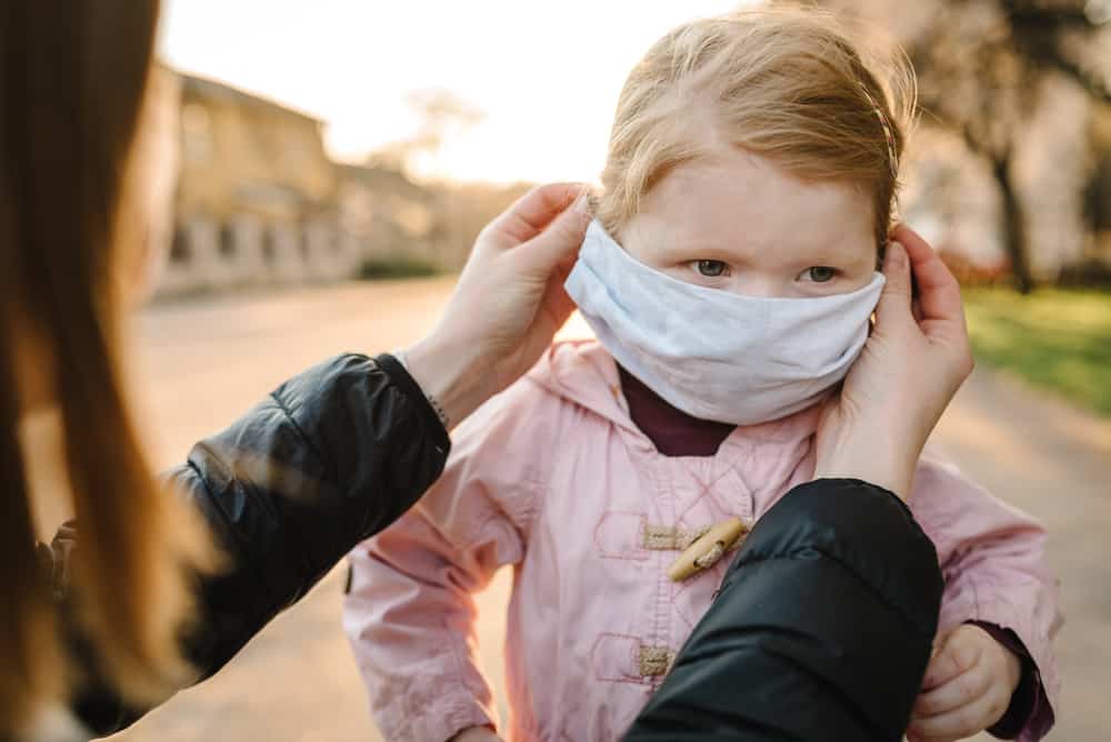 mom putting kids face mask on toddler