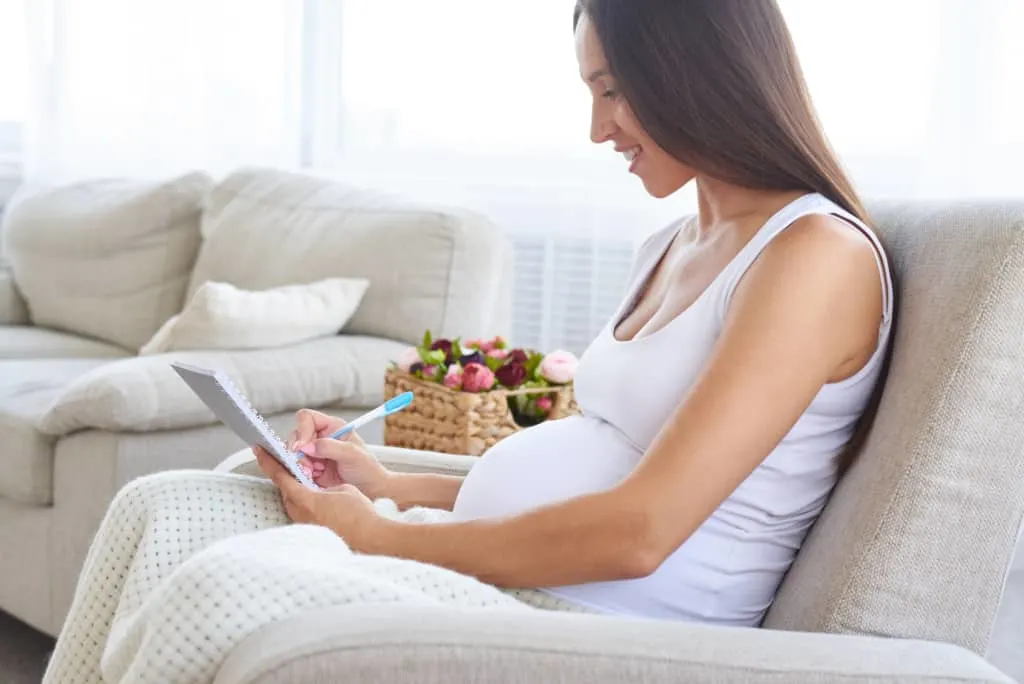 Pregnant woman uses notepad to list boy names that are one syllable.