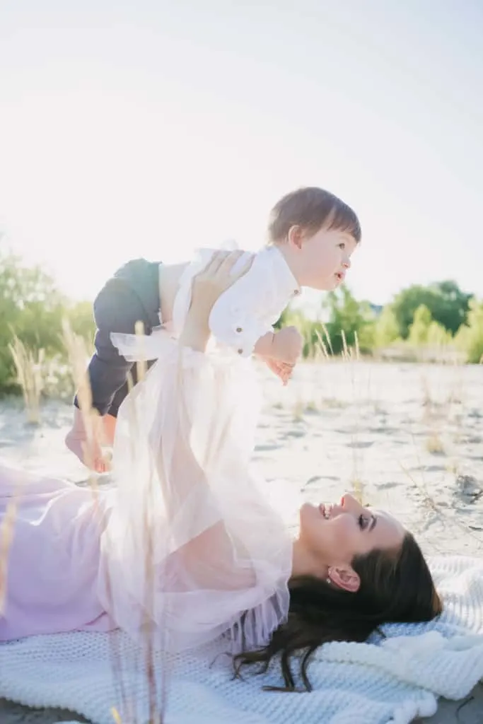 Mother holds baby above her on beach.