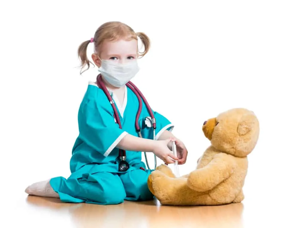 girl child wearing doctor costume with face mask attending to teddy bear