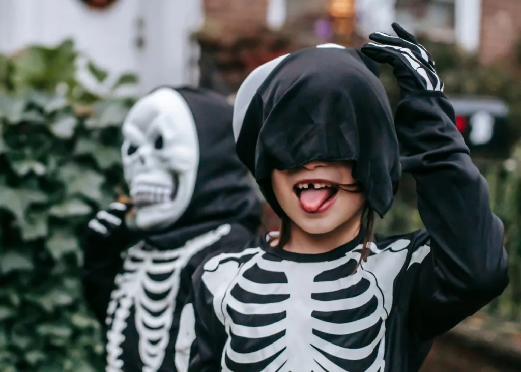 Two kids in skeleton costumes trick or treating.