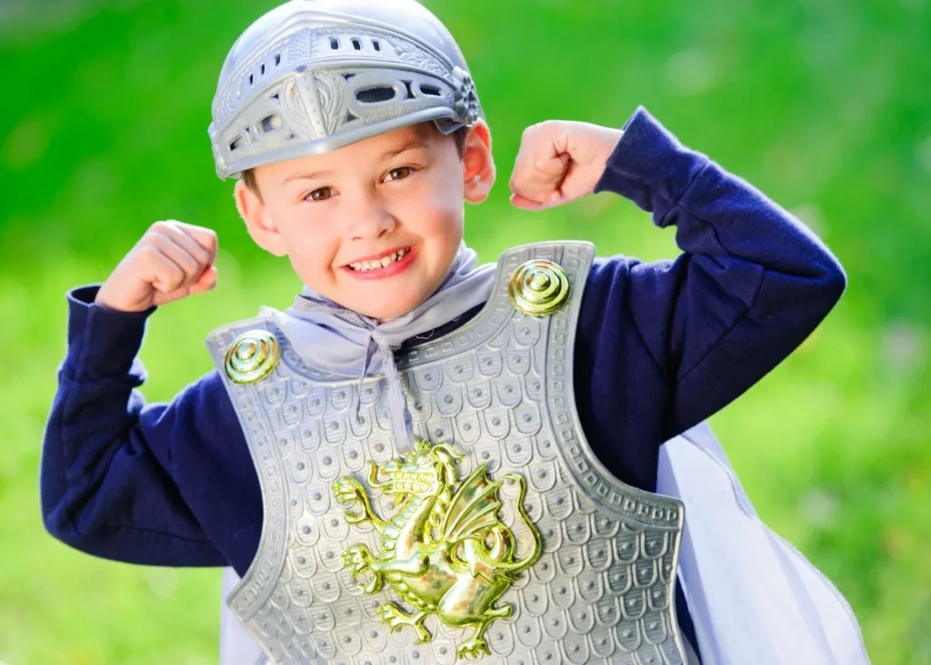 A young boy in a knight costume with a mask outside.