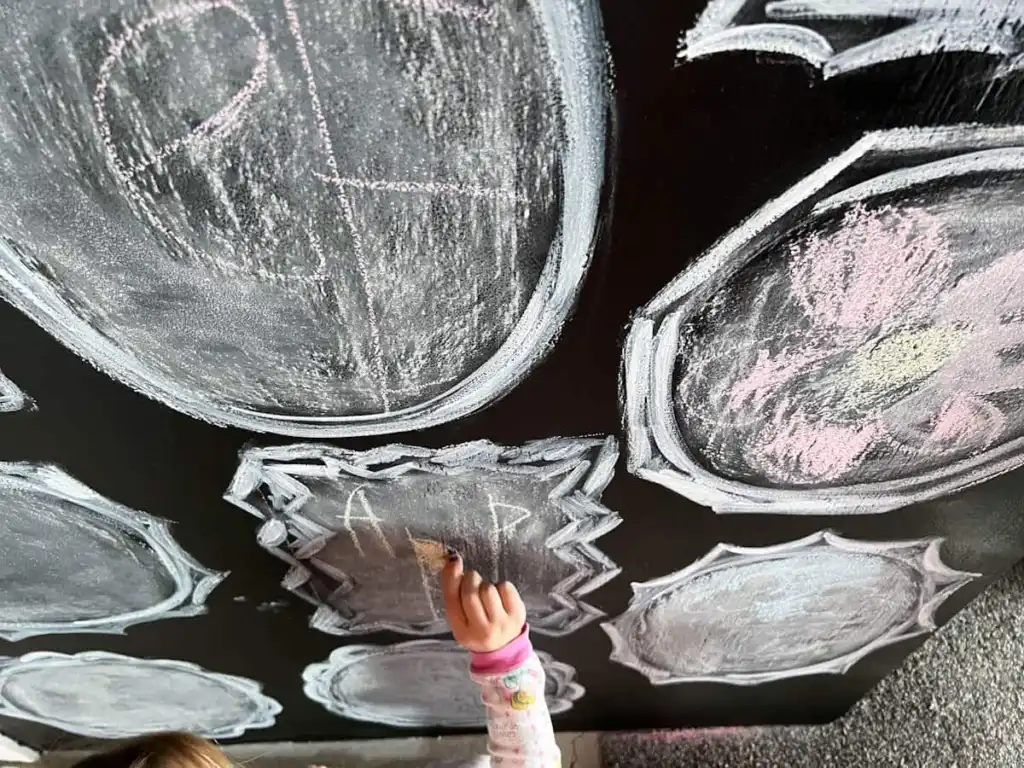 A little girl colors on a chalkboard wall.