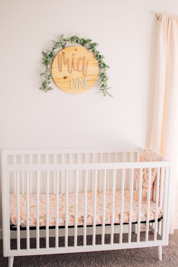 A wooden name sign that says "Mia Lynn" with greenery hanging over it.