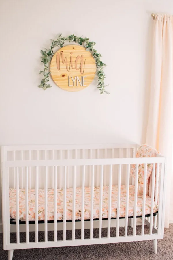 A wooden name sign that says "Mia Lynn" with greenery hanging over it.
