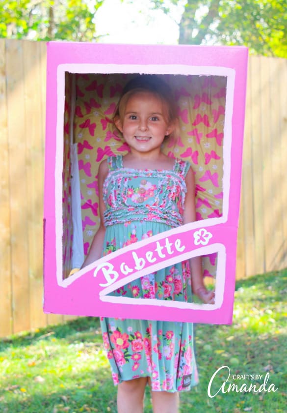 A girl in a pink cardboard doll box for Halloween.